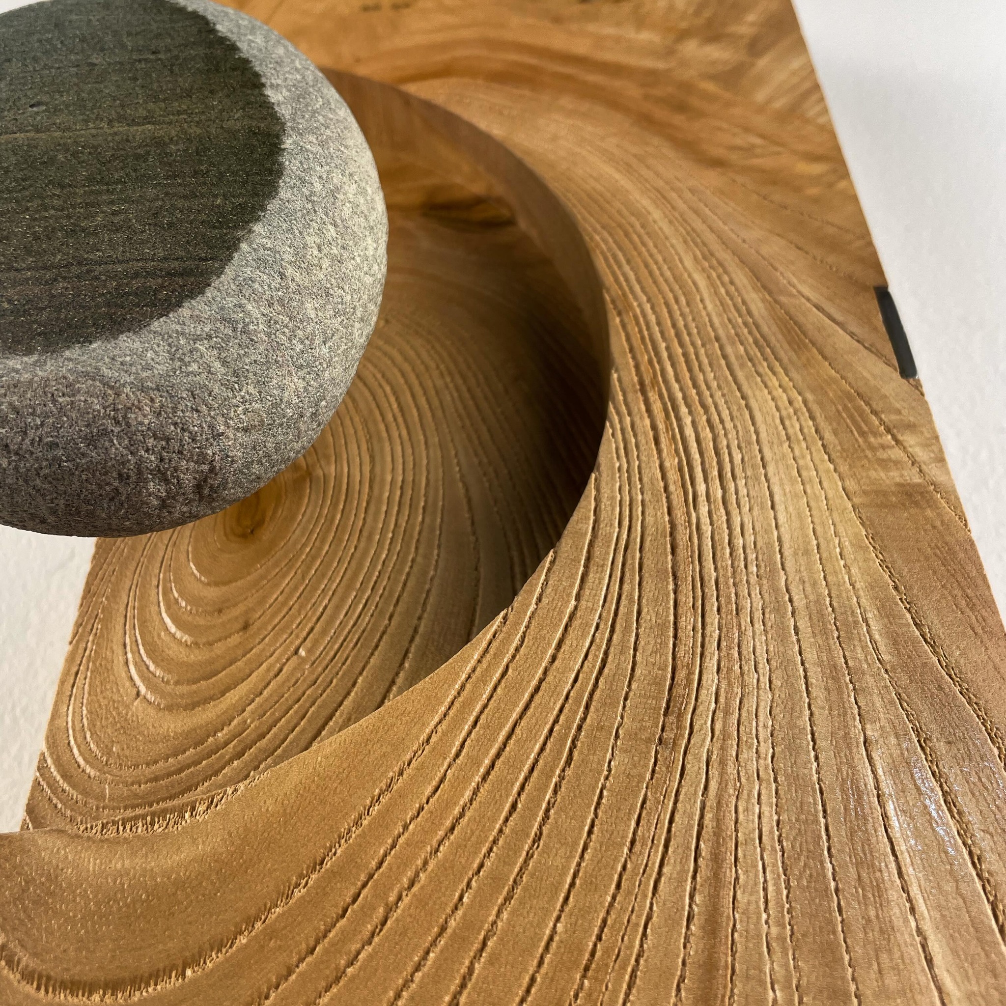 Carved wood wave sculpture cradling a river stone