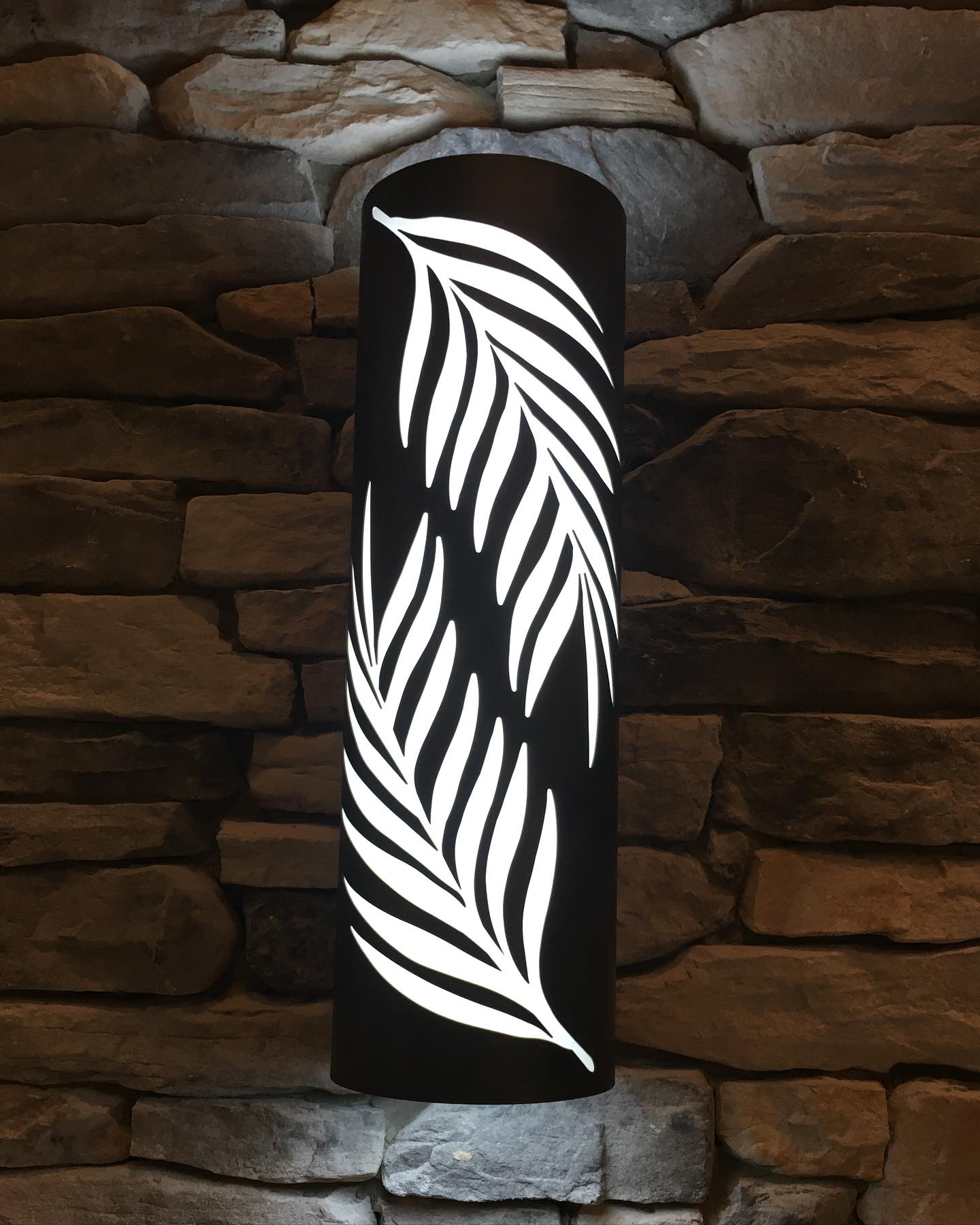 Laser-cut steel wall sconce with leaf pattern on stone wall