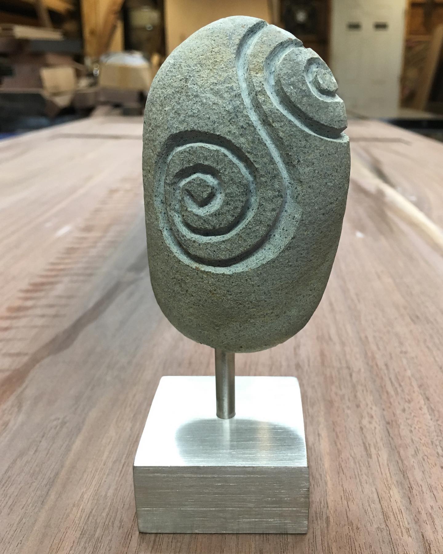 Carved river stone with spiral pattern on brushed steel pedestal